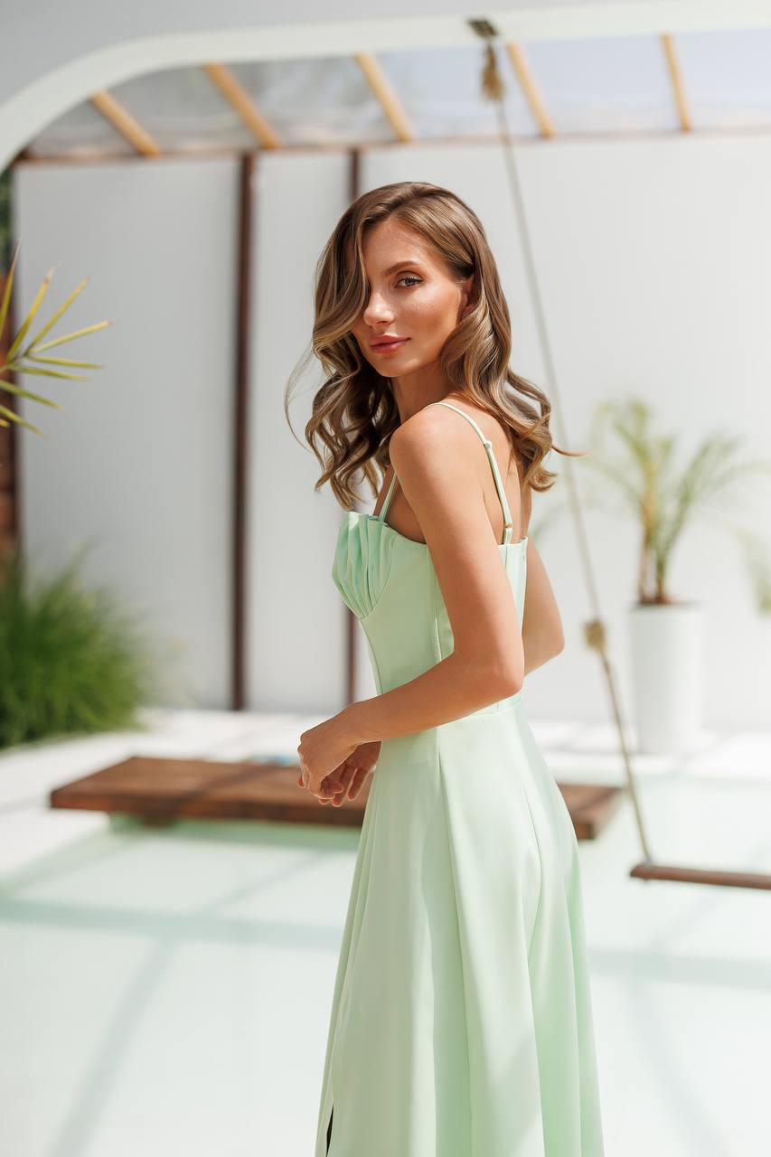 Woman in a light green dress standing outdoors with plants and a swing in the background