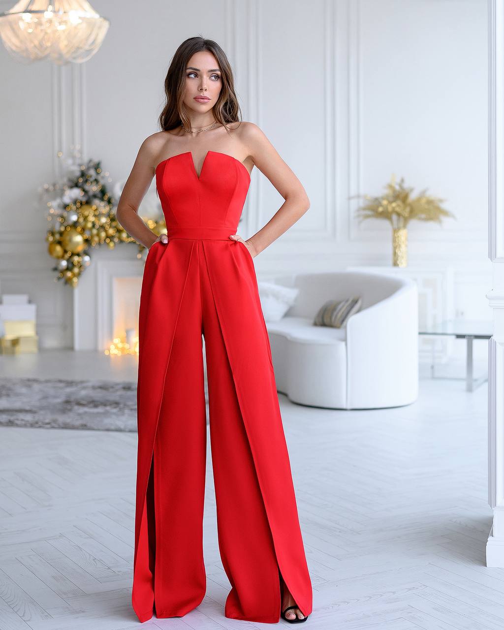 Woman wearing a red strapless jumpsuit in a stylish room with decor elements.