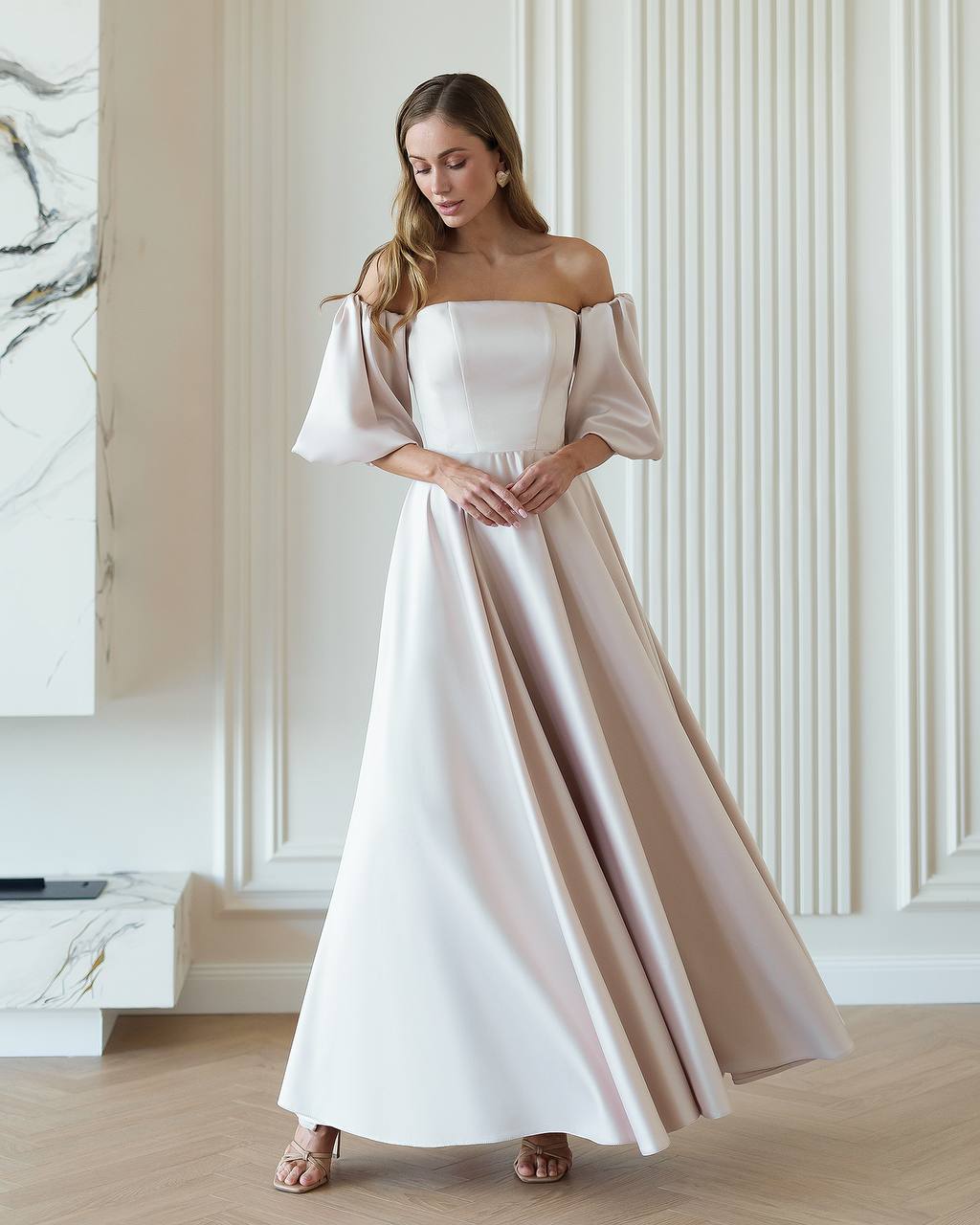 Woman wearing a white off-shoulder dress with pink sleeves in an elegant room.