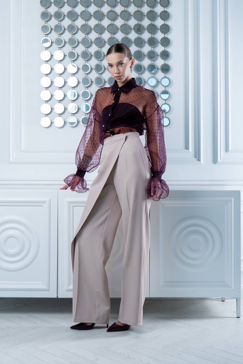 Model wearing a sheer top and wide-leg pants in a stylish interior setting.