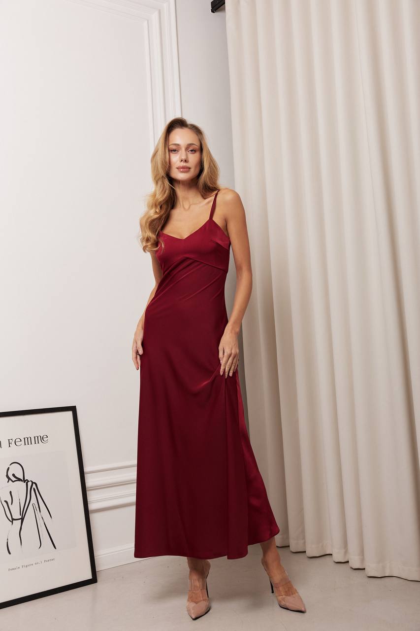Woman wearing a burgundy dress standing in a room with a white curtain and framed picture.