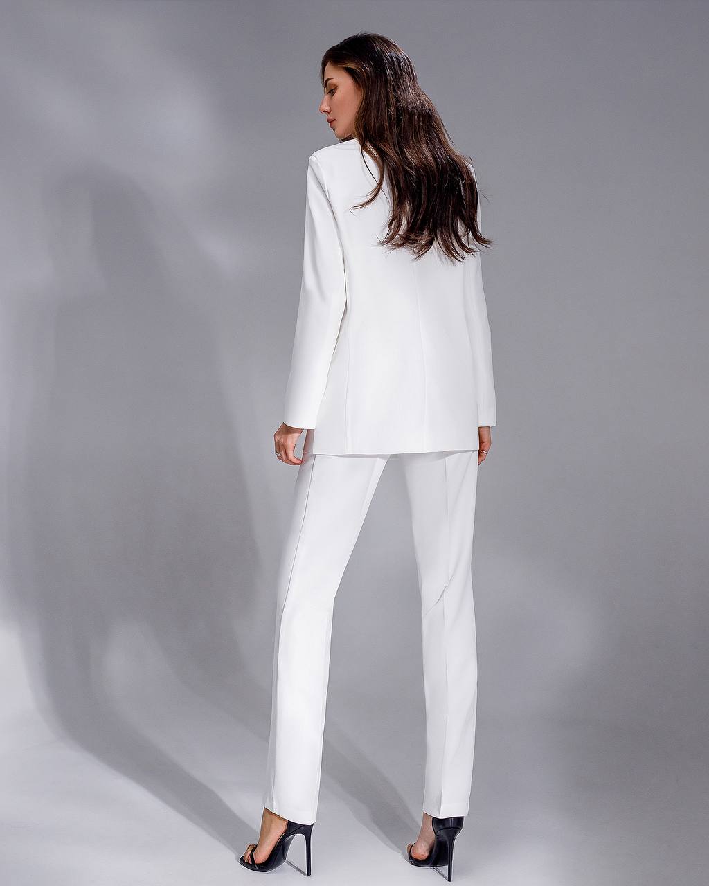 Woman wearing a white suit standing against a gray background