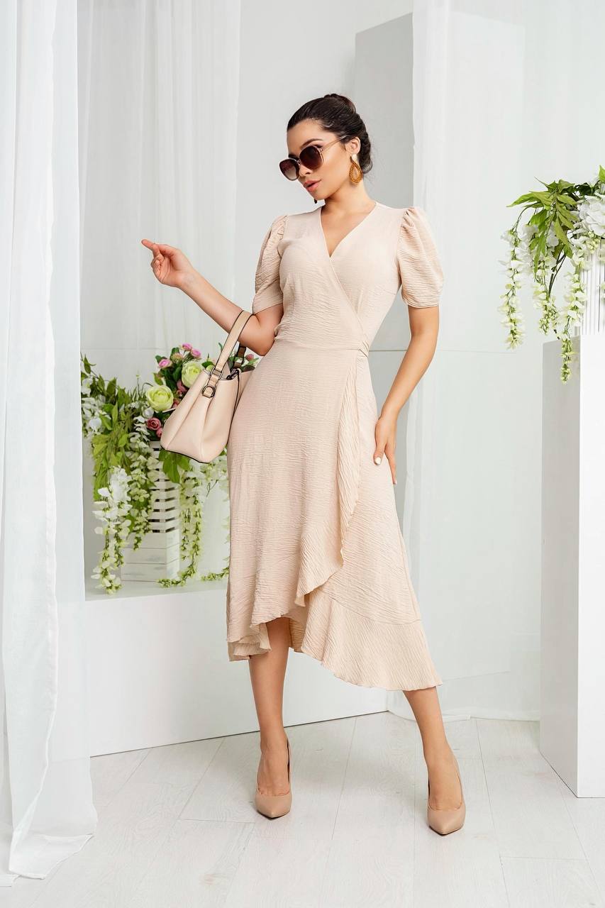 Woman in a beige dress standing in a bright room with plants.