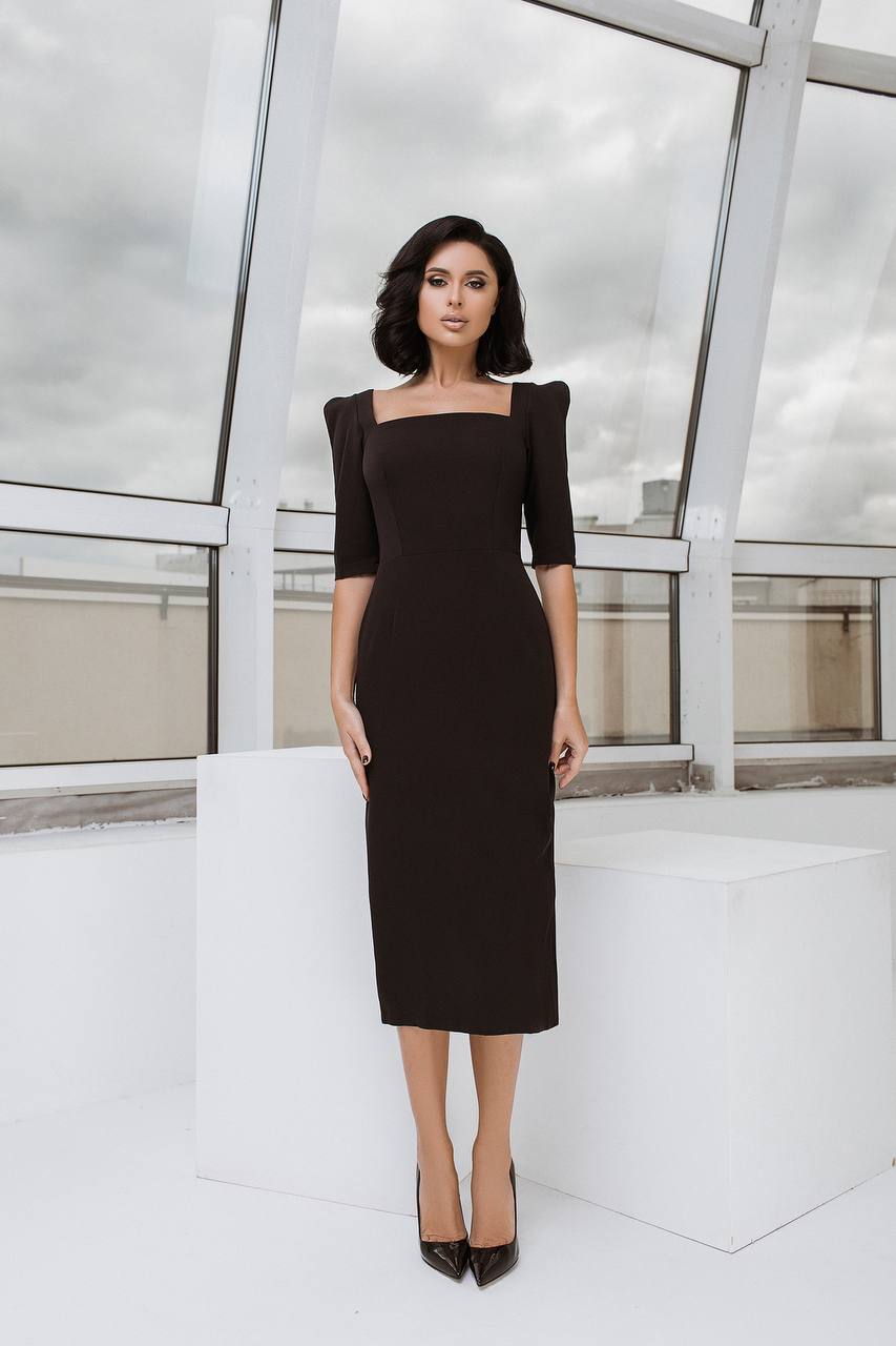 Woman wearing a black dress with puffed sleeves in an indoor setting with large windows.