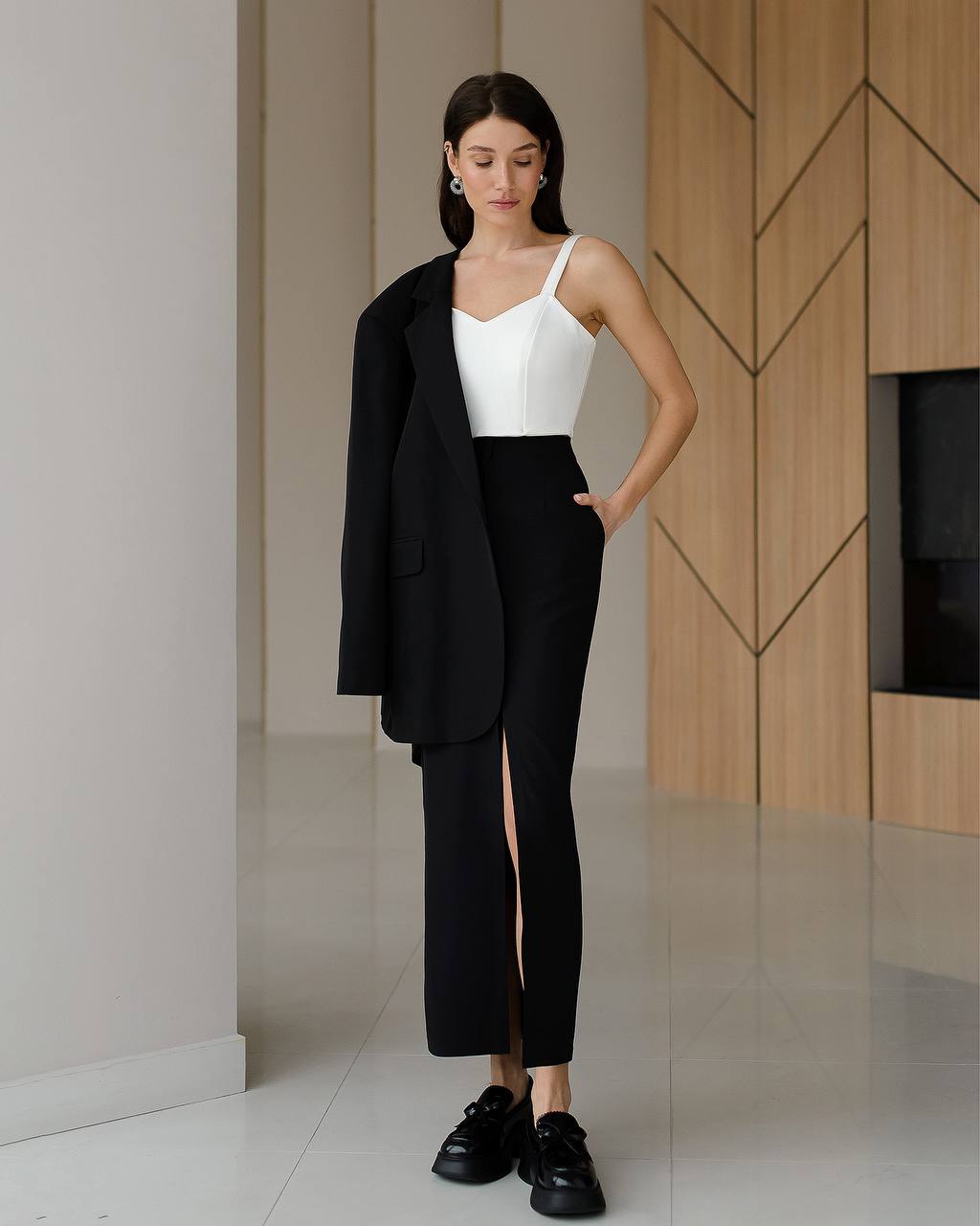 Woman wearing a black blazer, white top, and black pants in an indoor setting.