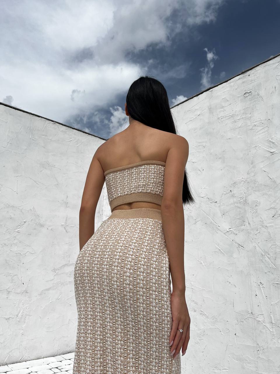 Woman wearing a strapless top and skirt set against a white wall with blue sky.