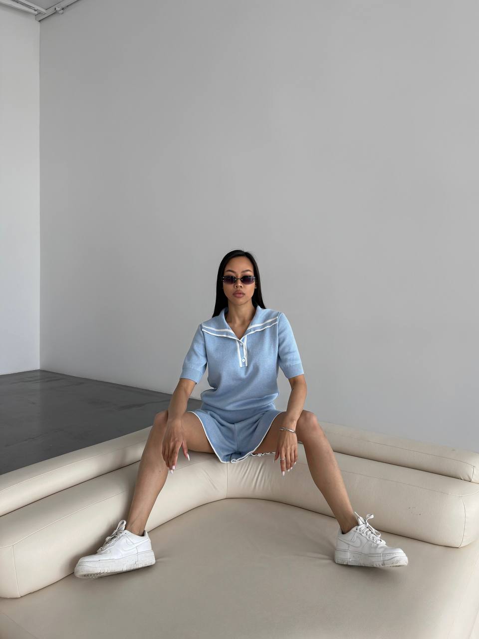 Person wearing a light blue dress sitting on a white bench against a plain wall.