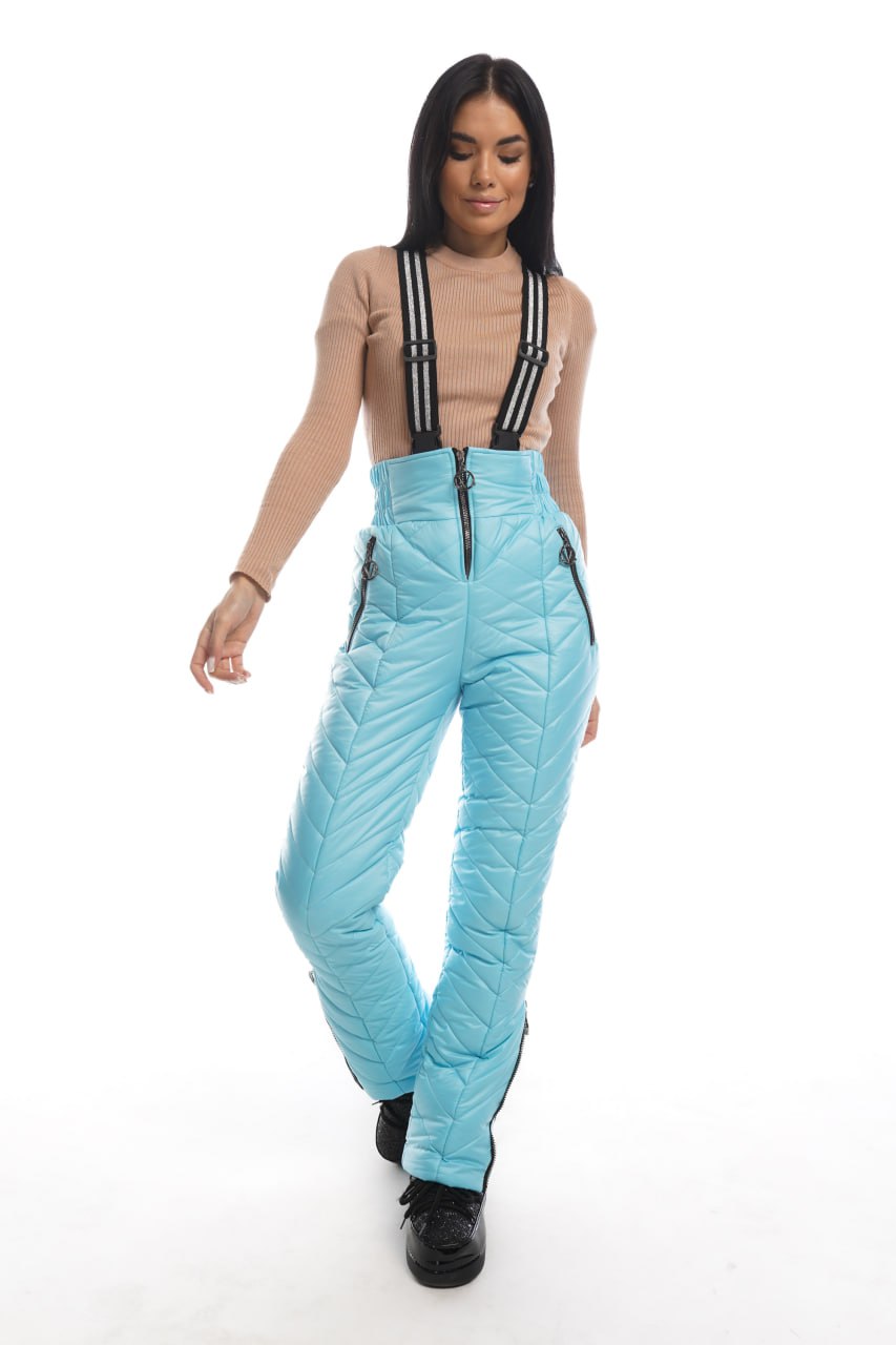 Woman wearing light blue ski pants with suspenders on a white background