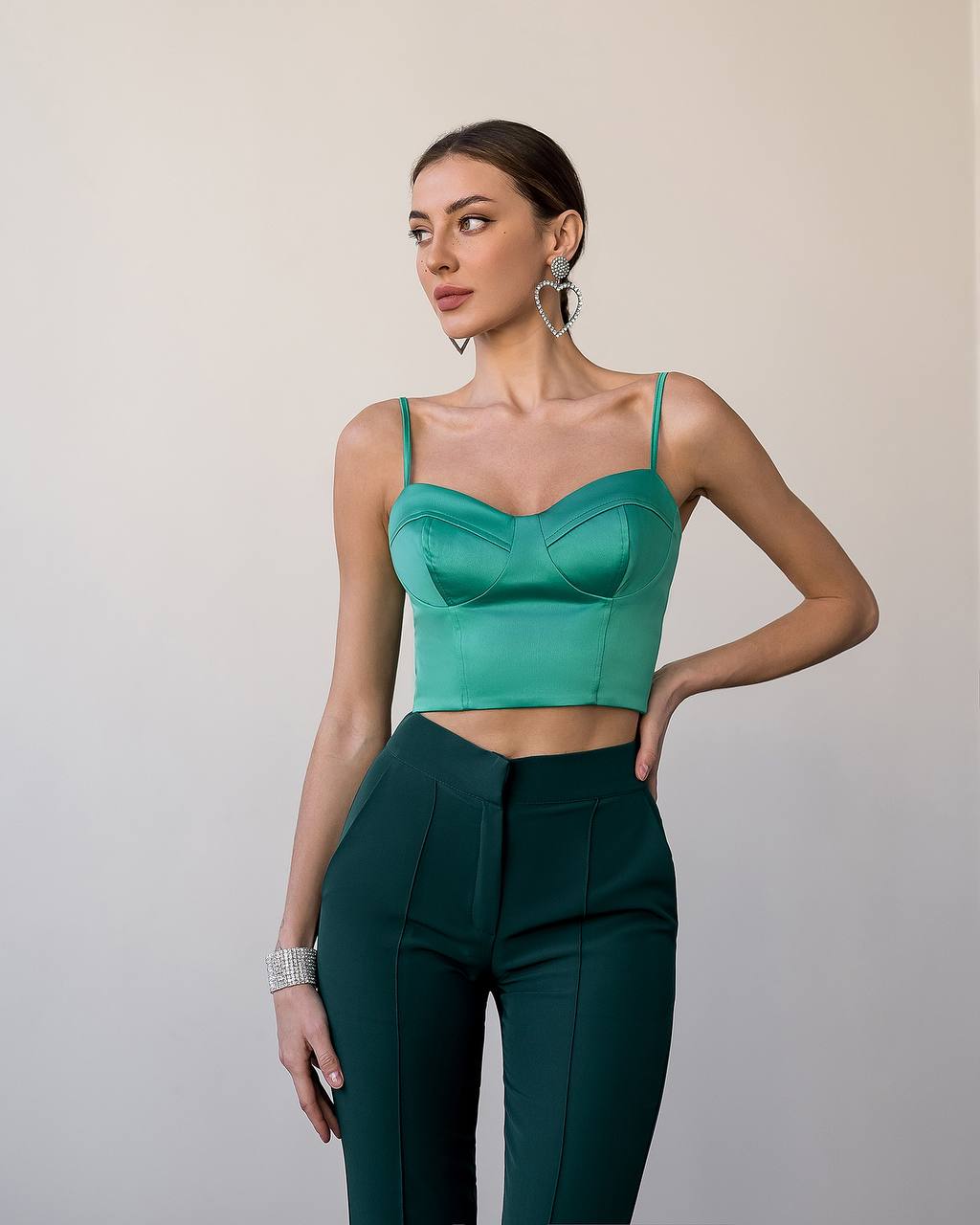 Woman wearing a green top and dark green pants against a plain background