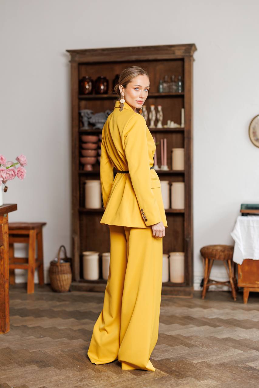 Woman in a yellow suit standing in a room with wooden furniture and decor.