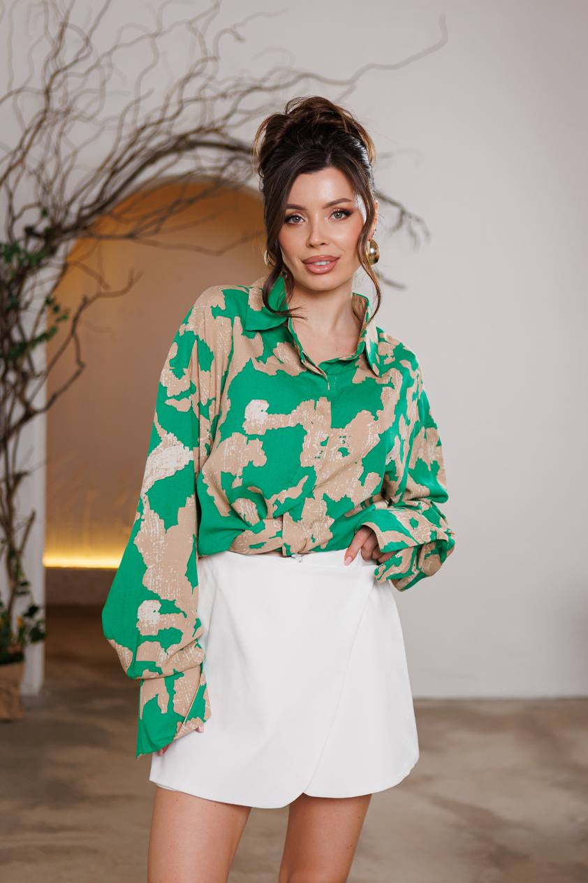 Woman wearing a green and beige patterned blouse with white shorts in an indoor setting.