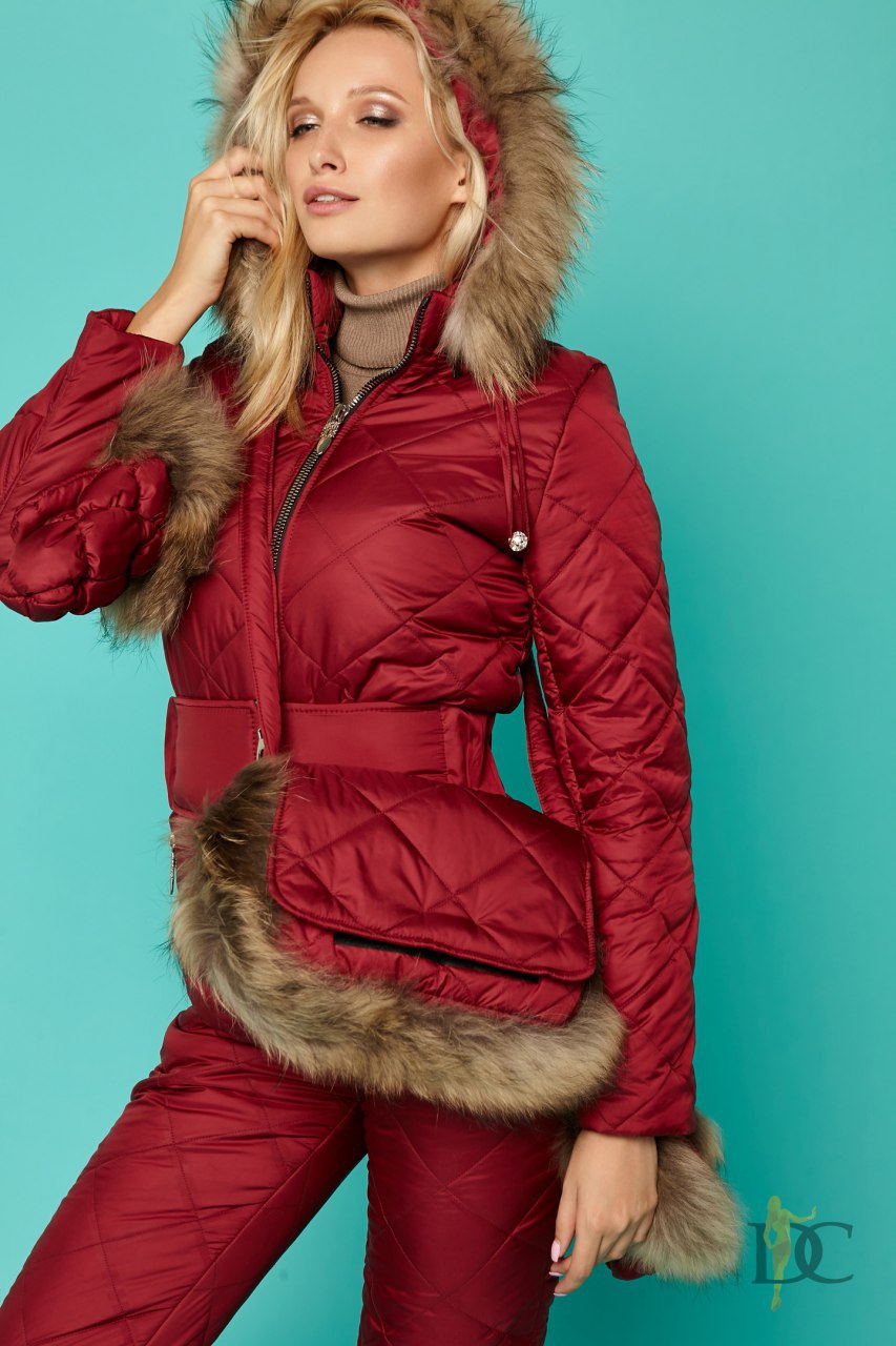 Woman wearing a red puffer jacket with fur trim against a teal background