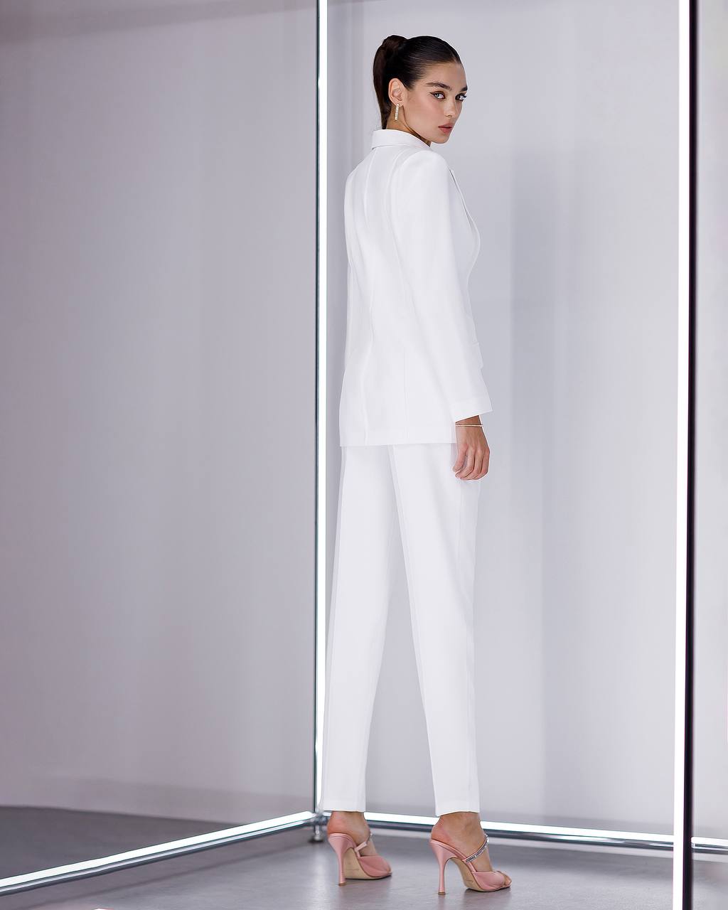 Woman wearing a white outfit standing in front of a mirror.