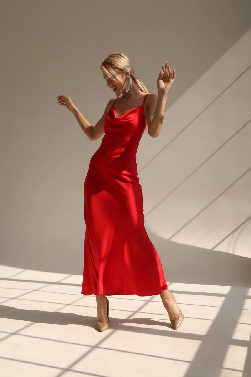 Woman in a red dress standing in a sunlit room with shadows on the floor.