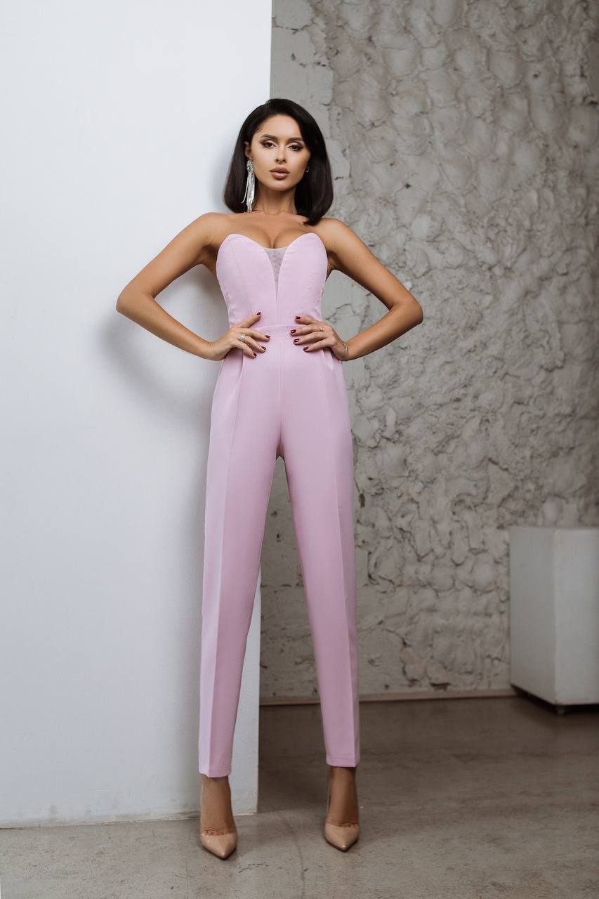 Woman wearing a pink jumpsuit against a textured wall.