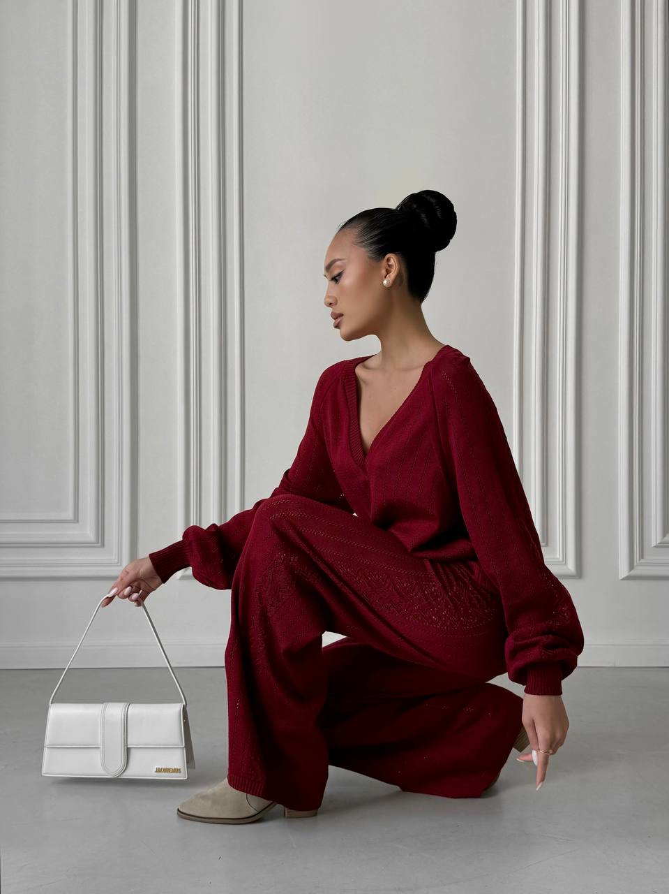 Woman in a red outfit holding a white handbag against a gray wall.