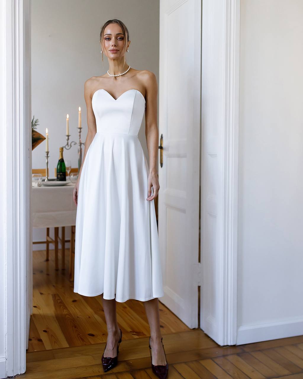 Woman wearing a white strapless dress standing in a room with wooden flooring.