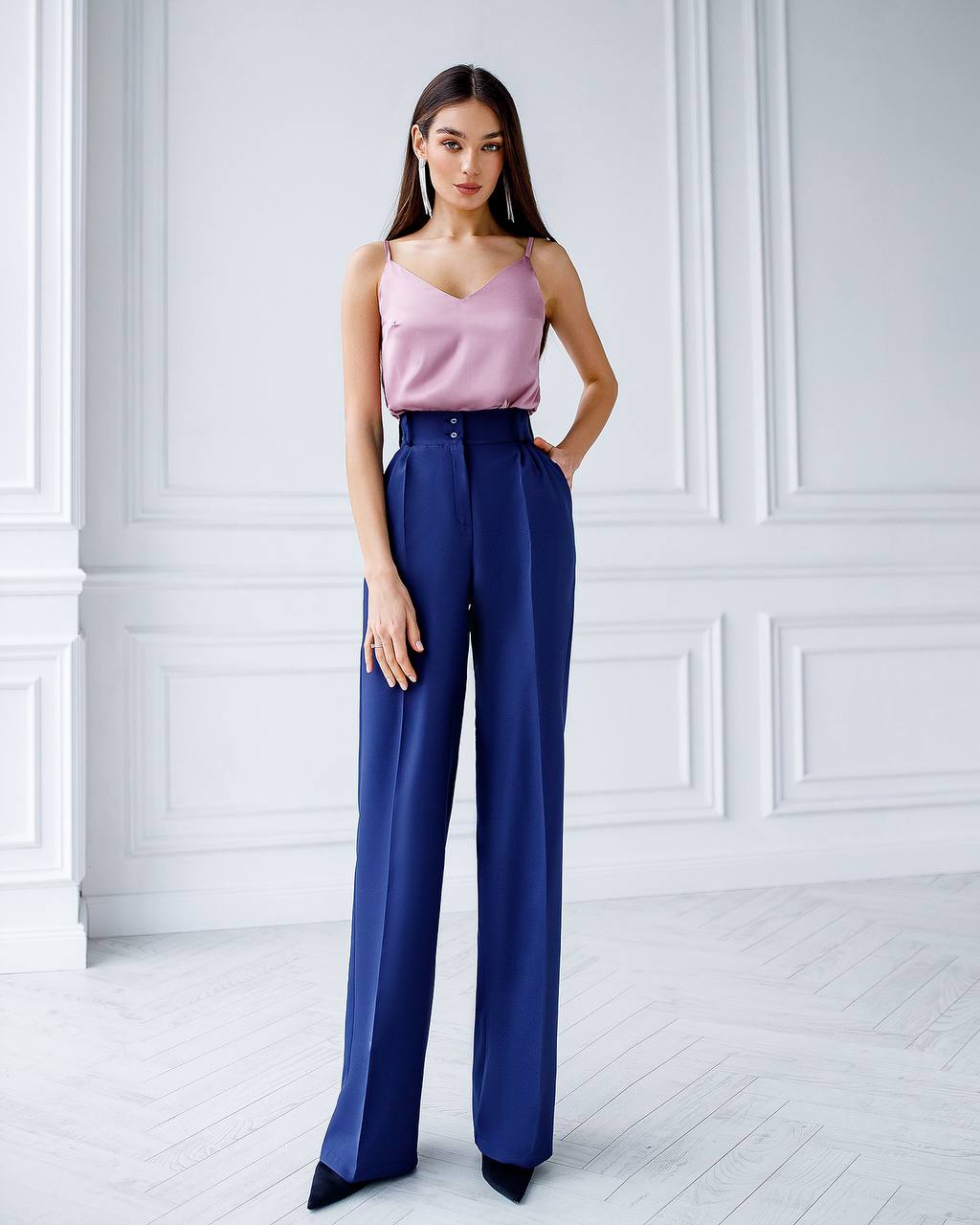 Woman wearing a pink top and blue pants in a white room