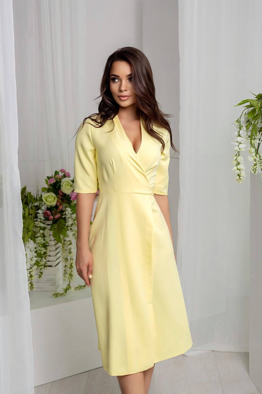 Woman wearing a yellow dress standing in a room with white curtains and floral decorations.