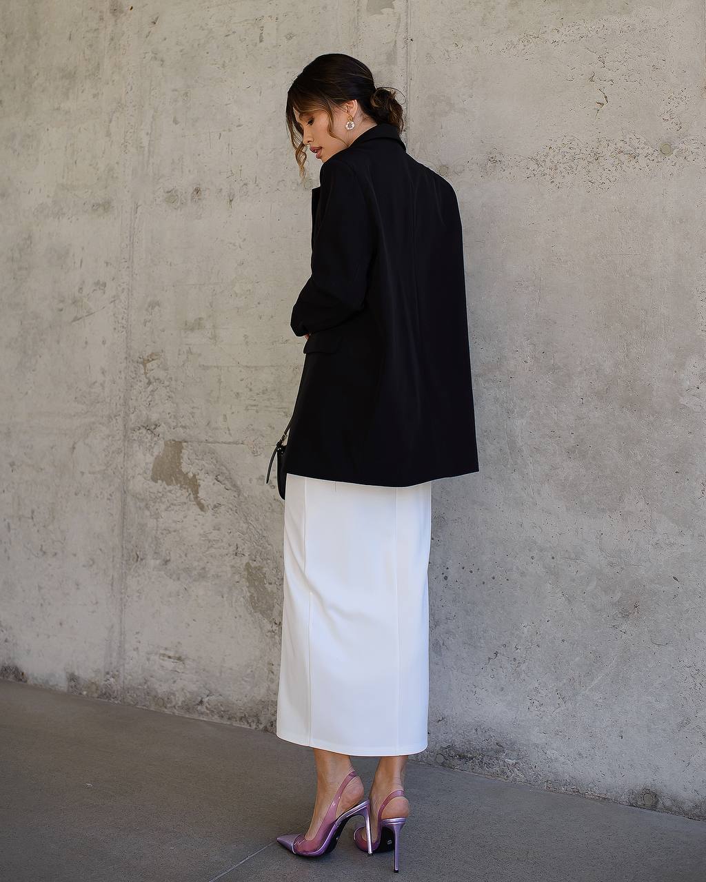 Woman wearing a black blazer and white skirt against a concrete wall.