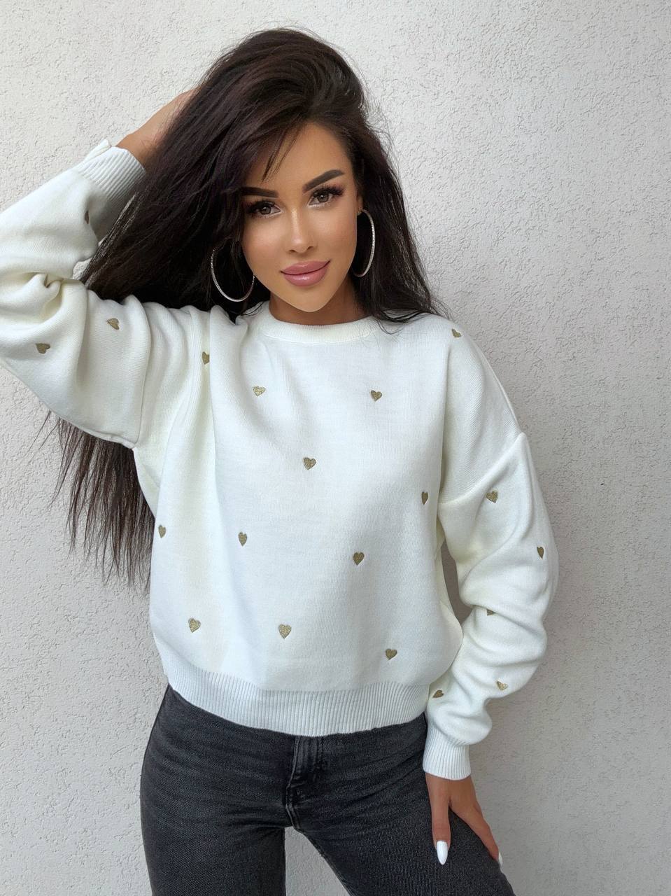 Woman wearing a white sweater with heart patterns against a plain background
