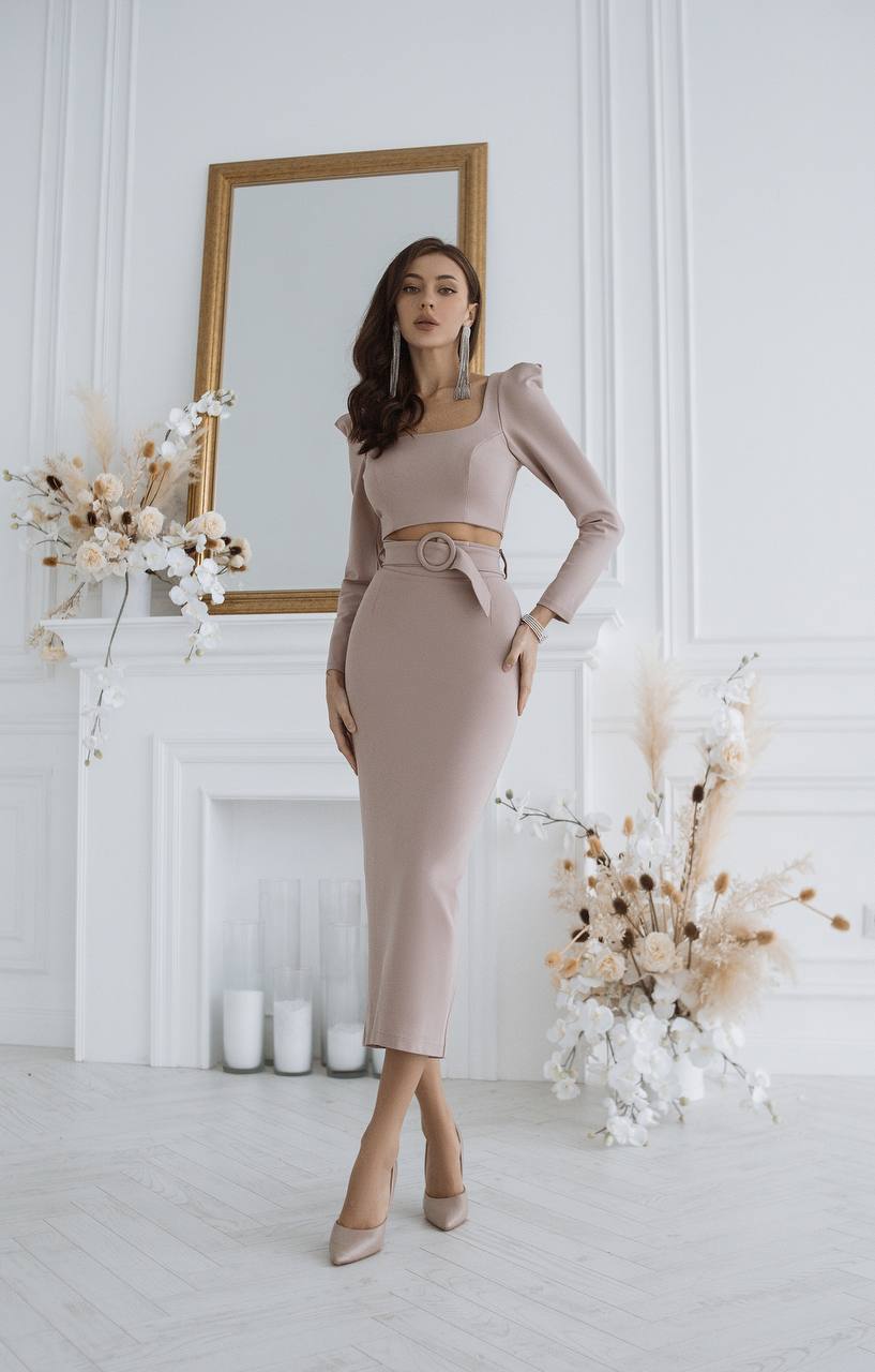 Woman in a beige outfit standing in a stylish room with decor elements.