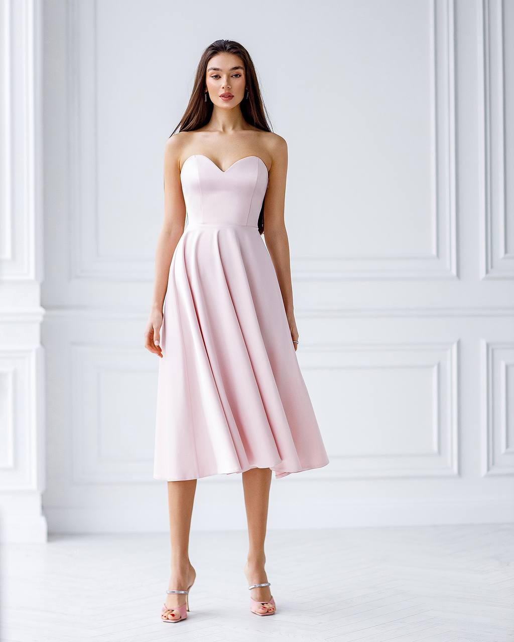 Woman wearing a pink strapless dress against a white wall