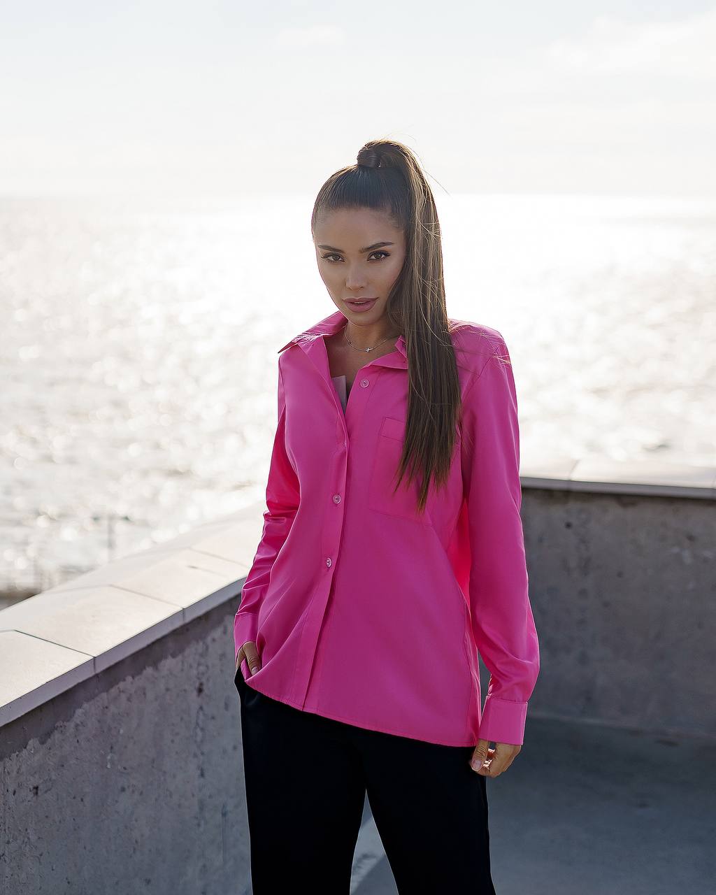 Woman wearing a bright pink shirt standing on a rooftop with a light background
