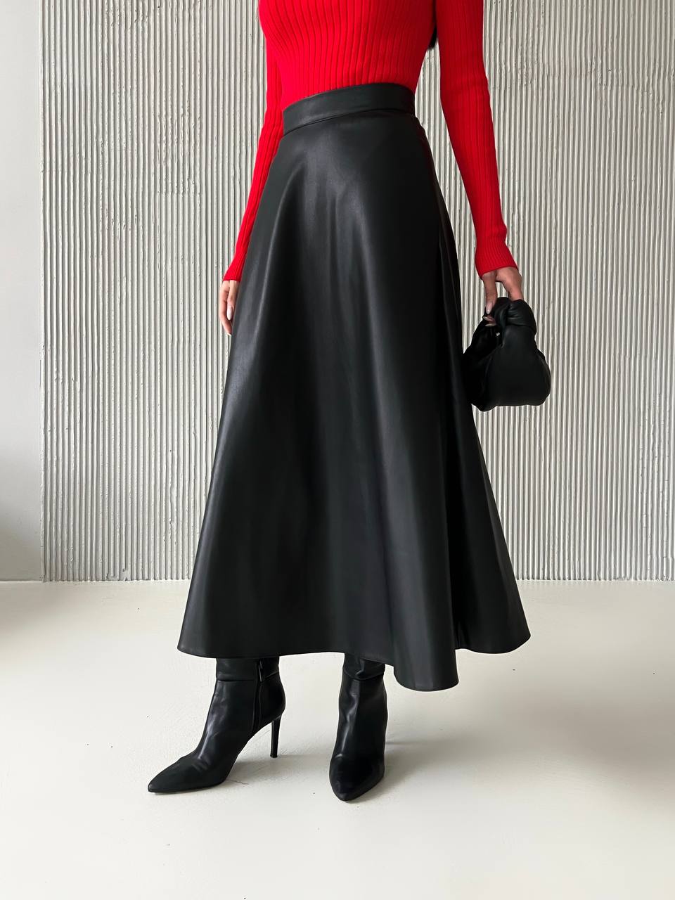 Person wearing a red sweater, black leather skirt, and black boots against a striped wall.