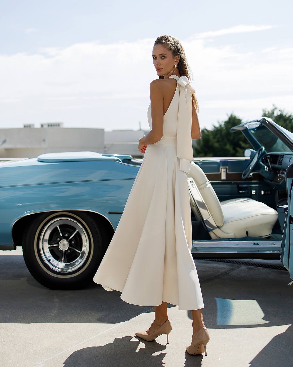 Woman in a white dress standing next to a vintage car