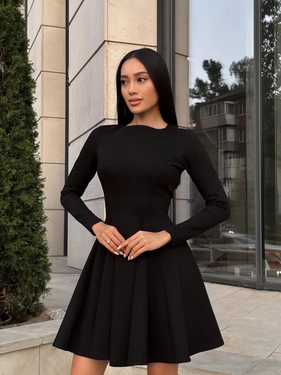 Woman wearing a black dress standing outdoors near a building.