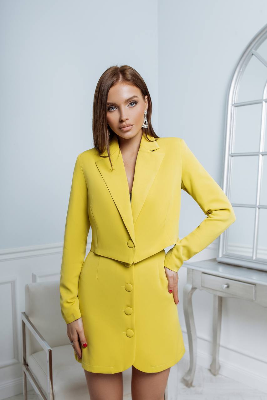 Woman wearing a yellow suit in a bright room with a mirror.