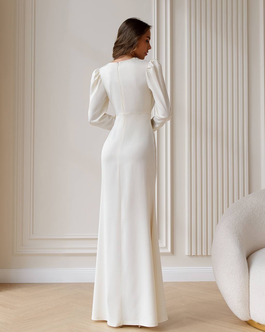 Woman in a long white dress standing in a room with decorative walls.