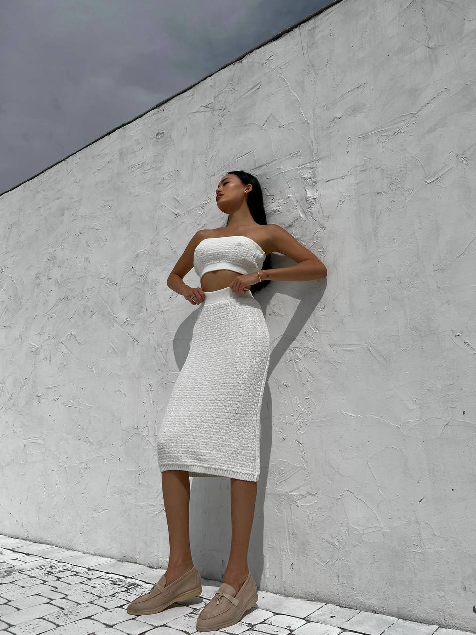 Woman in a white strapless dress standing against a light gray wall.