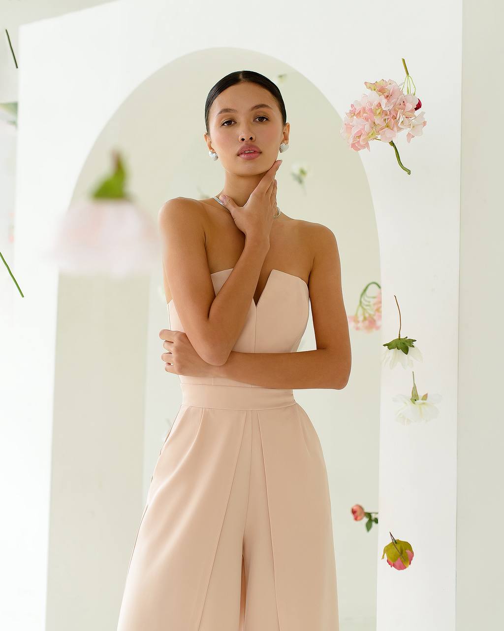 Woman in a light pink dress standing in front of a decorative mirror with flowers.