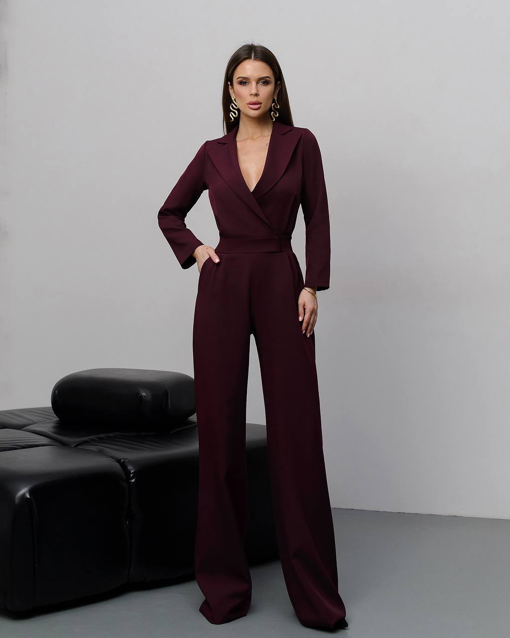 Woman wearing a burgundy jumpsuit against a gray background