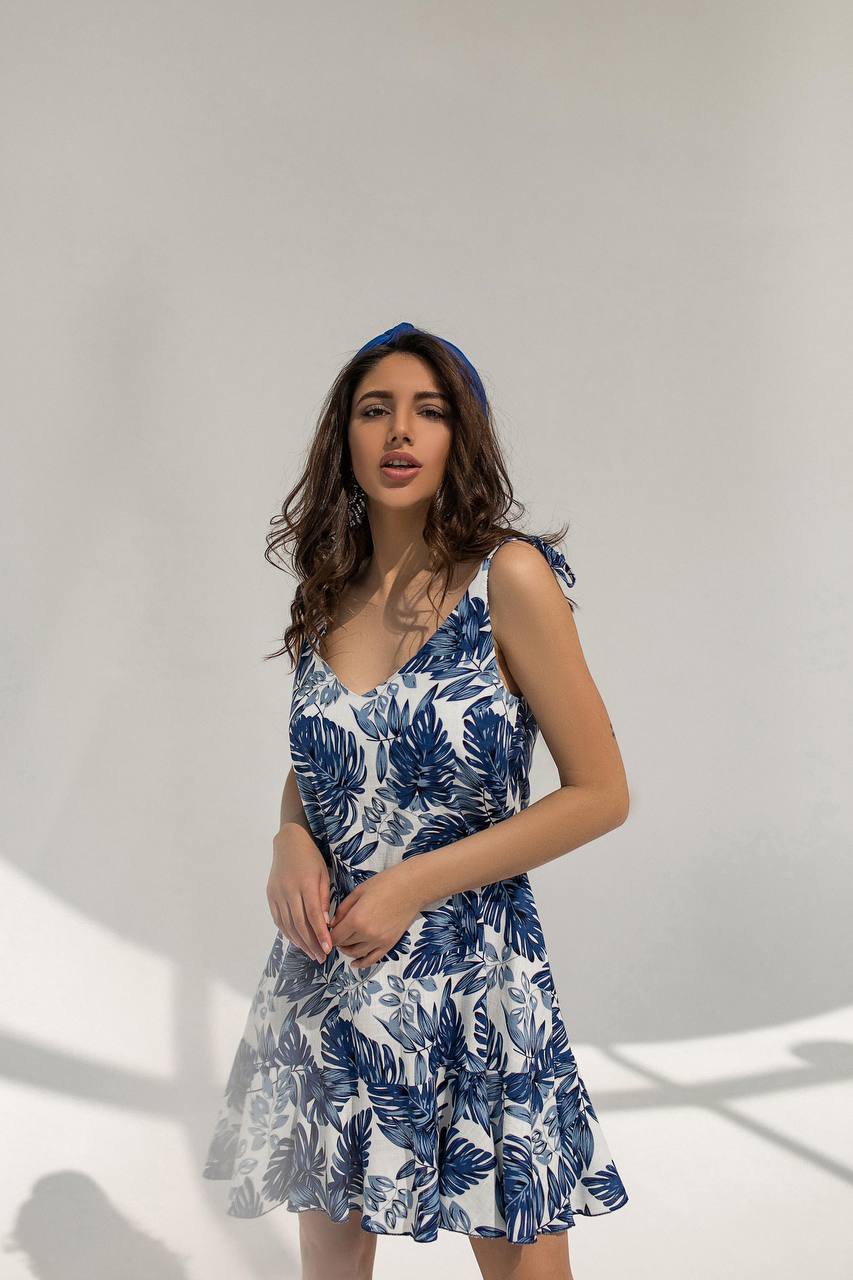 Woman wearing a blue and white floral dress against a plain background