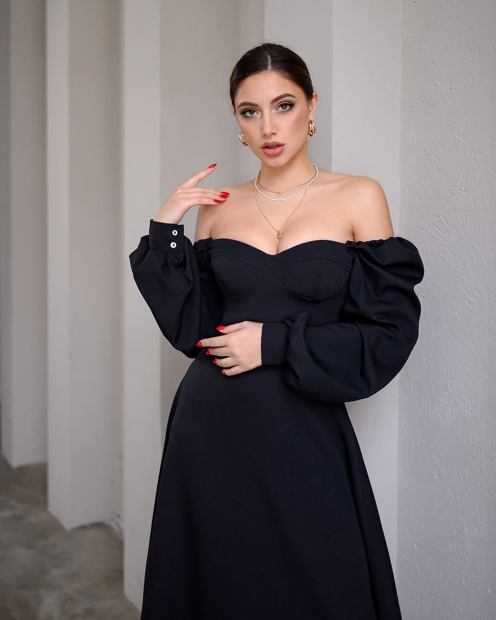 Woman wearing a black off-shoulder dress against a plain wall.