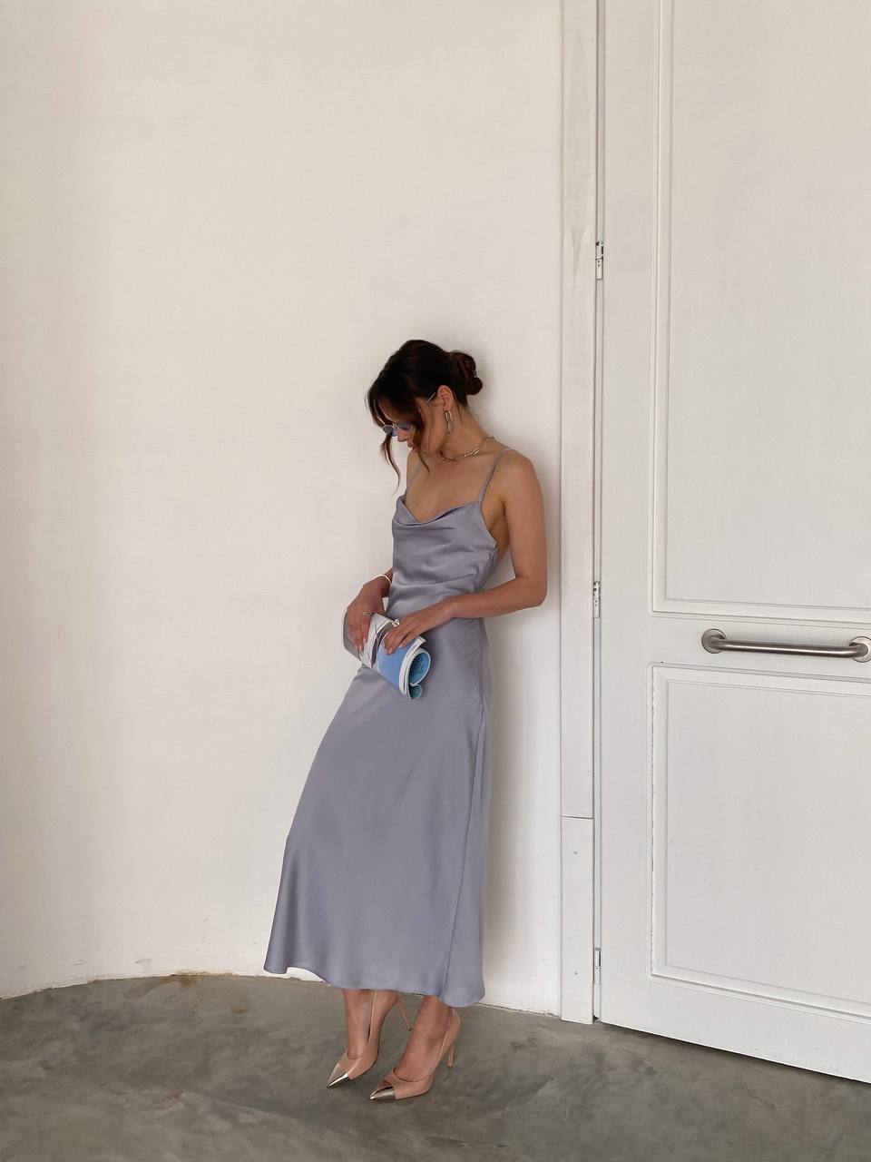 Woman in a light gray dress standing against a white wall.
