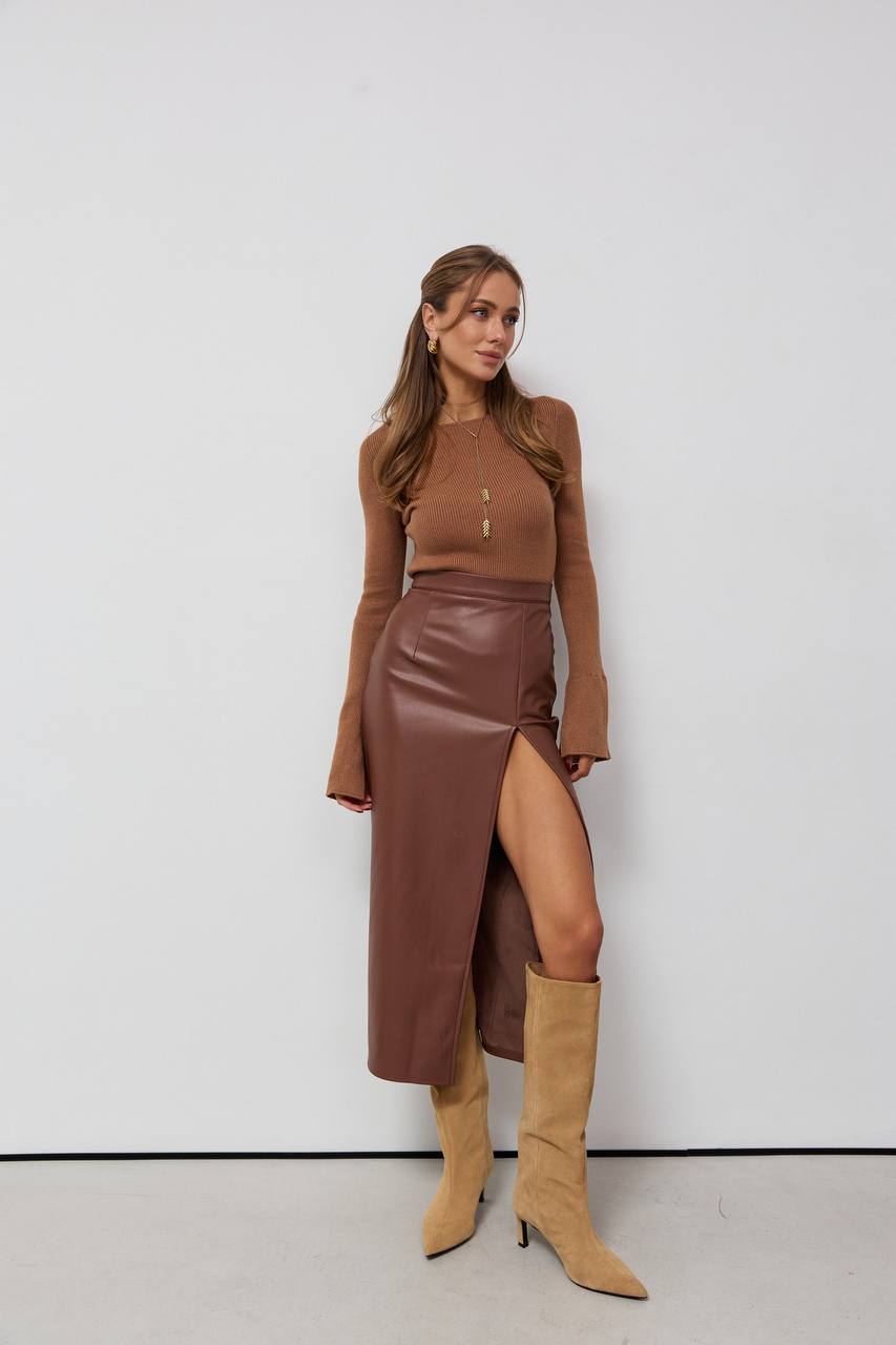 Woman wearing a brown outfit with a leather skirt and knee-high boots against a white background
