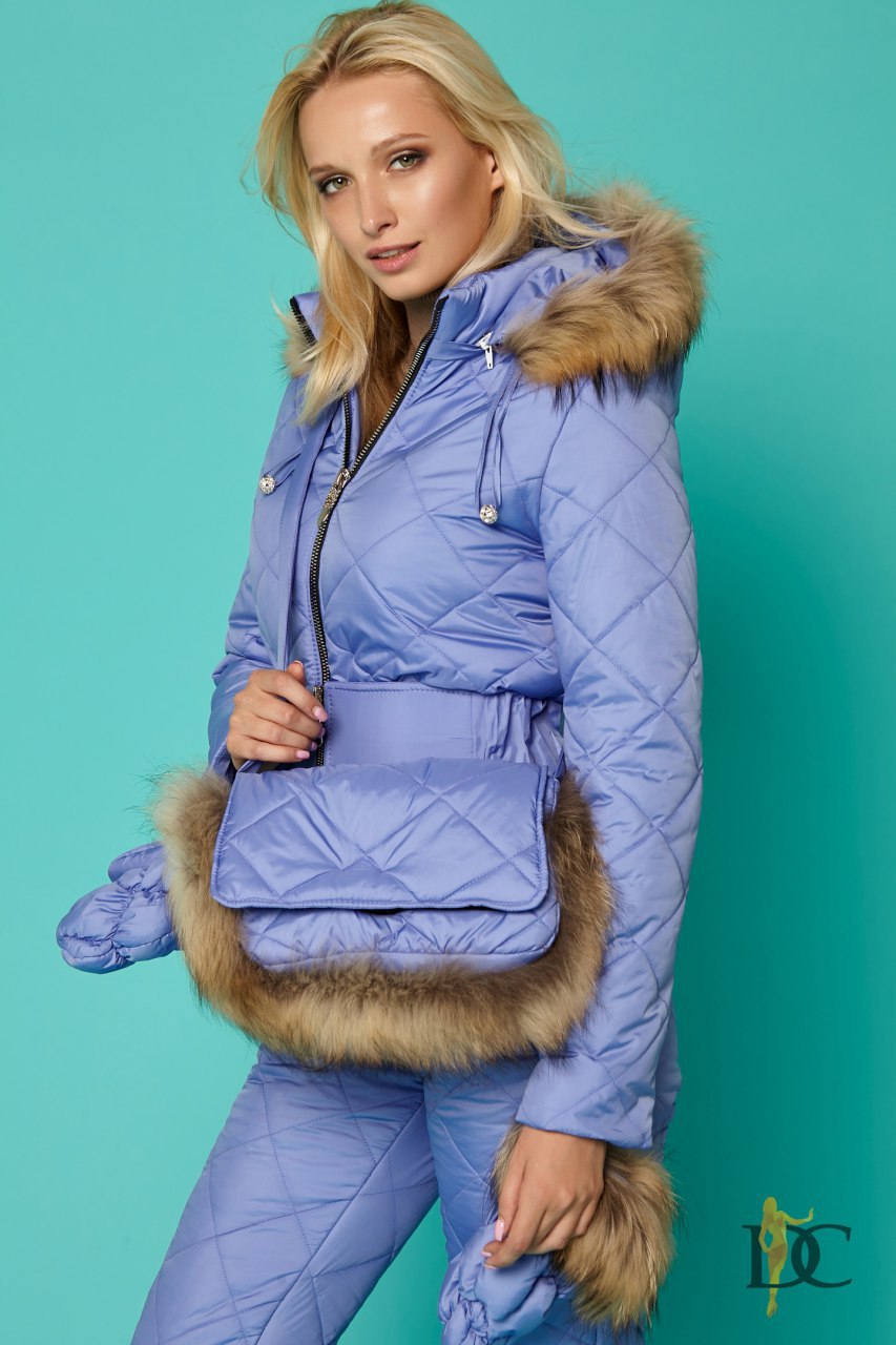 Woman wearing a blue quilted jacket with fur trim against a teal background