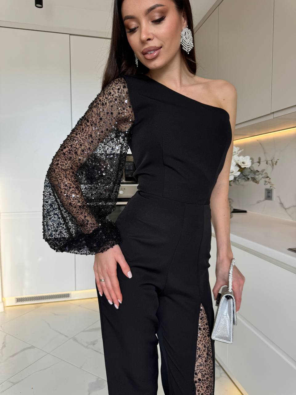 Woman wearing a black one-shoulder outfit with sheer sleeves in a kitchen setting