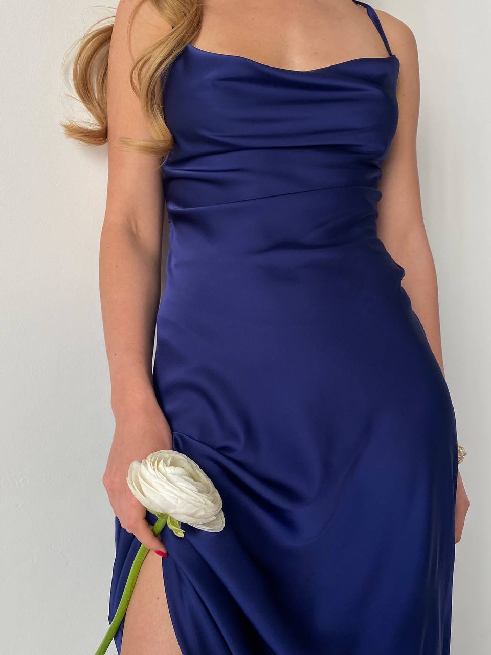 Woman wearing a blue dress holding a white flower against a plain background