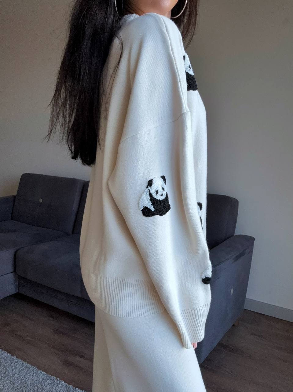 Person wearing a white sweater with panda designs in a room with a gray couch.
