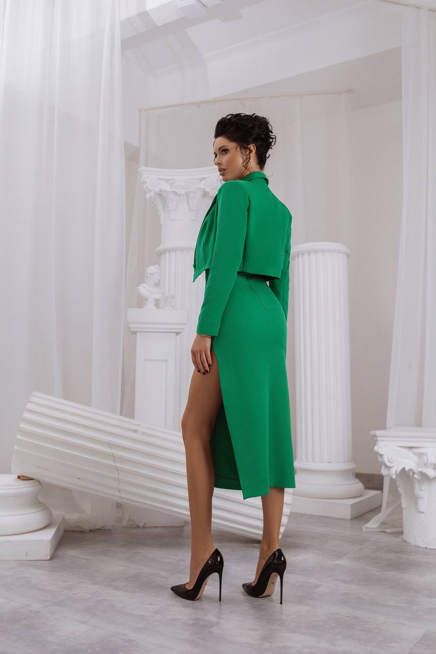 Woman in a green outfit standing in a classical room with white columns.