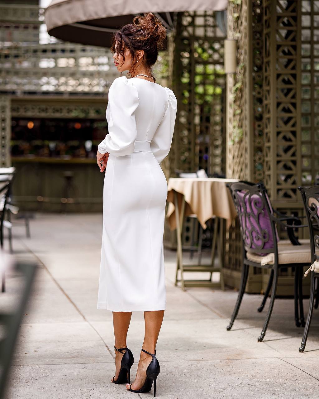 Woman in a white dress standing outdoors with tables and chairs in the background