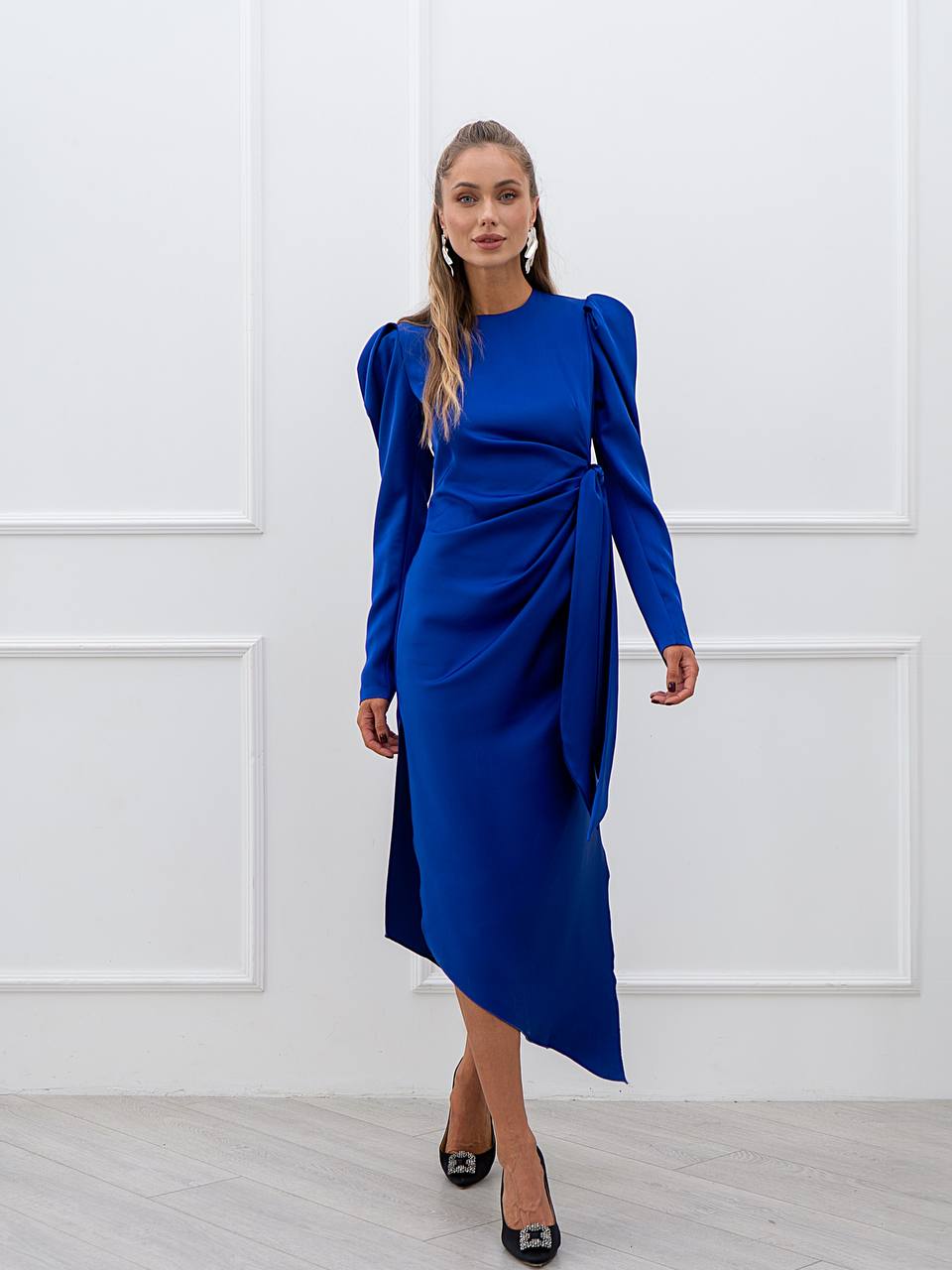 Woman wearing a blue dress against a white paneled wall