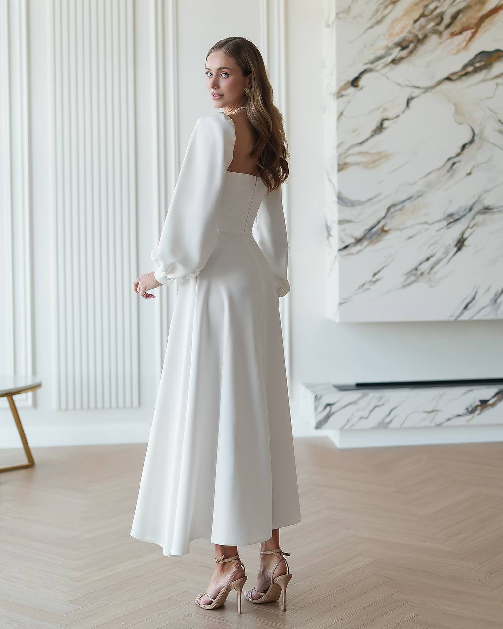 Woman in a white dress standing in a room with marble wall.