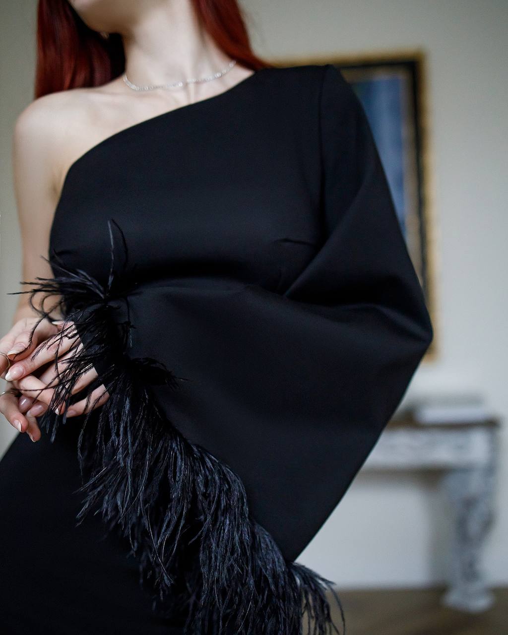 Black one-shoulder dress with feather details worn by a person indoors.