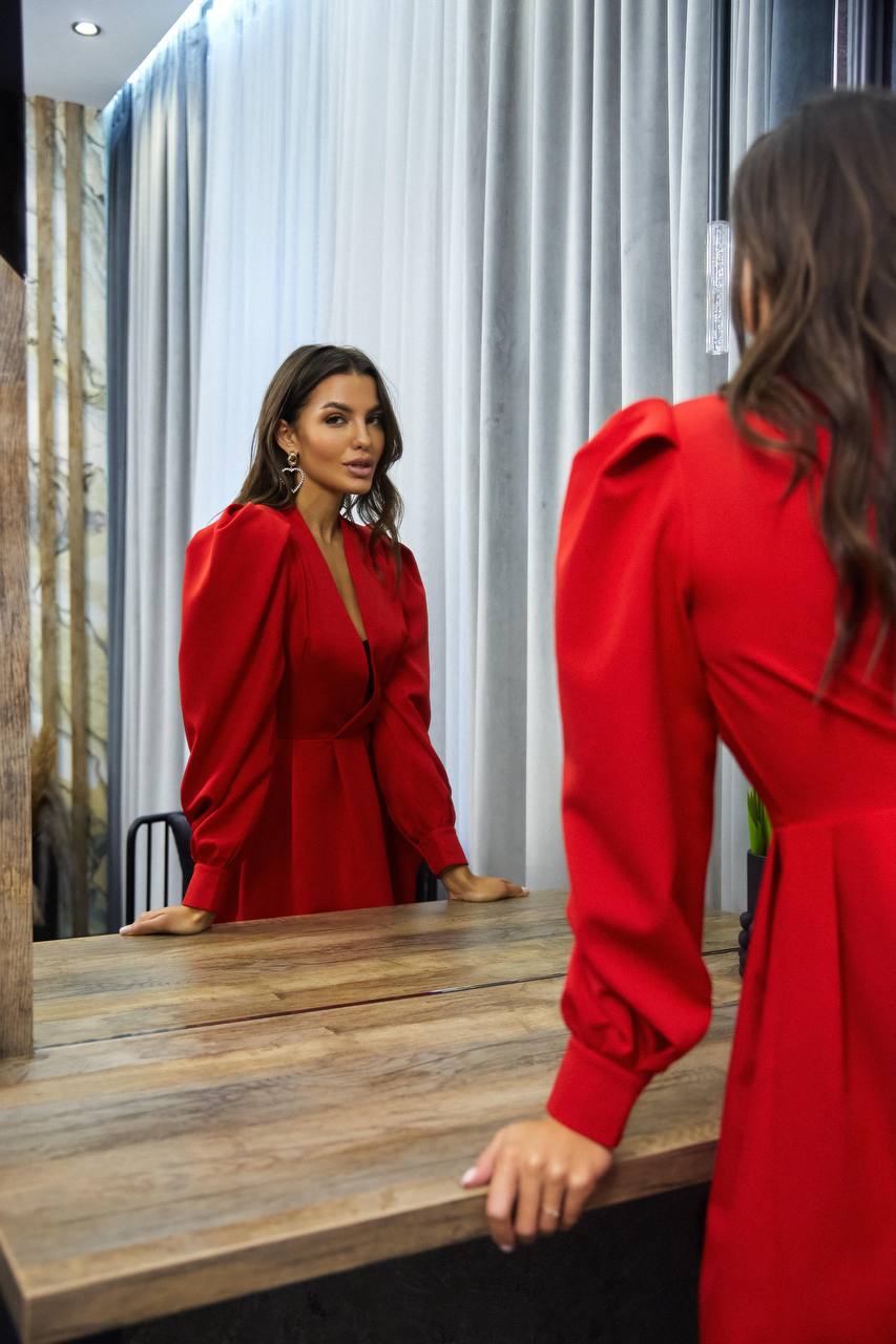 Woman in a red dress looking at herself in a mirror.